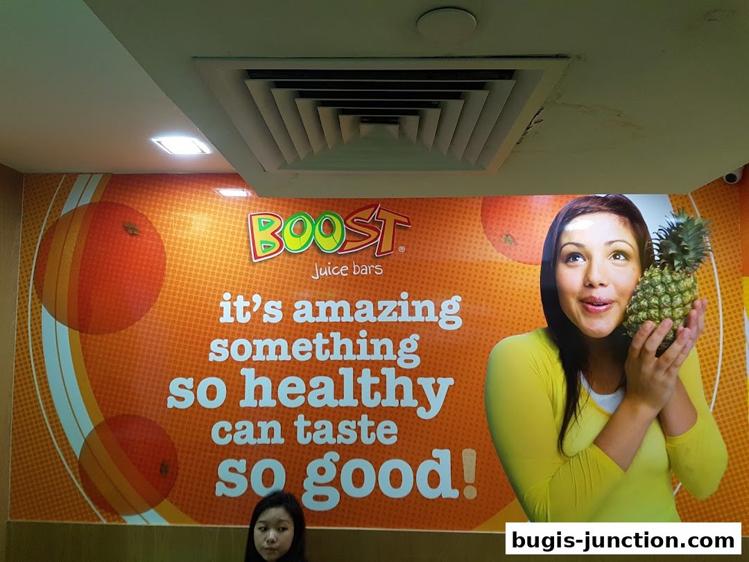 A vibrant wall mural at Boost Juice featuring the brand logo, a slogan, and a woman holding a pineapple.