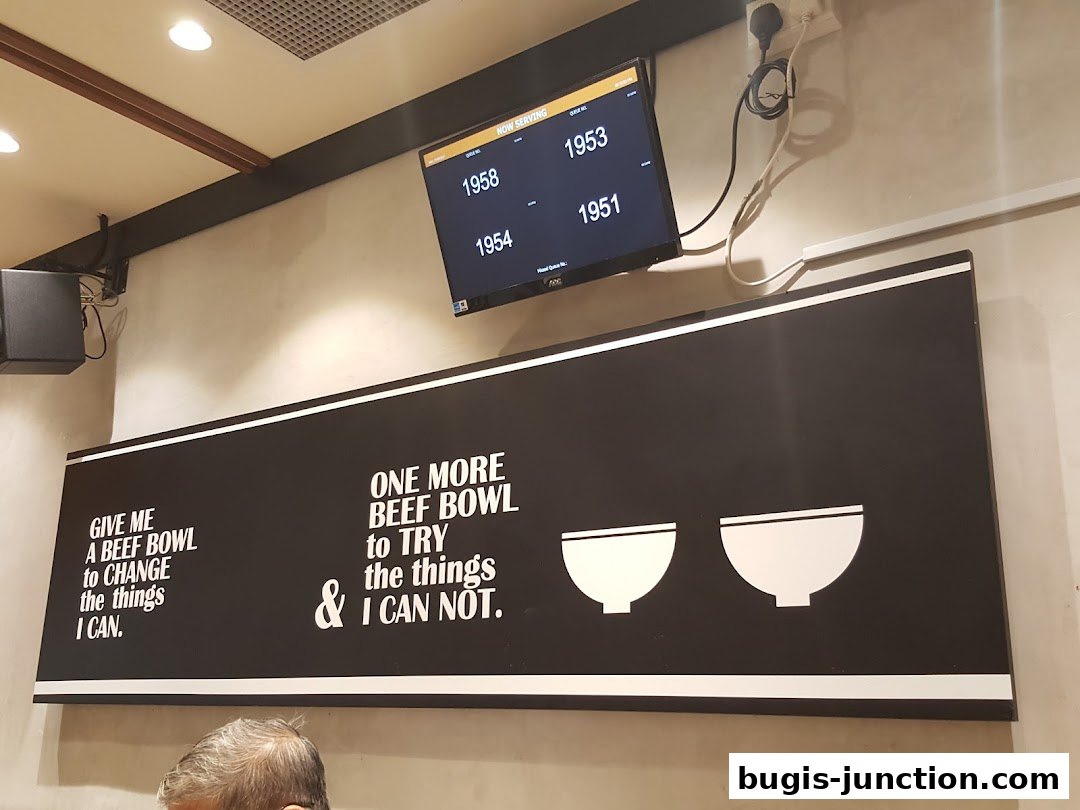 A Yoshinoya restaurant interior with a digital queue display and motivational text on the wall.