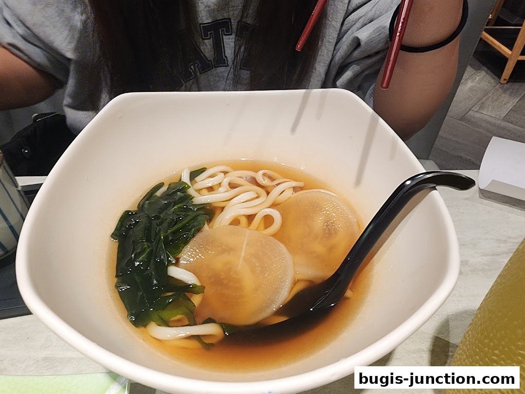 A bowl of udon noodles with seaweed and radish in broth, served with chopsticks.