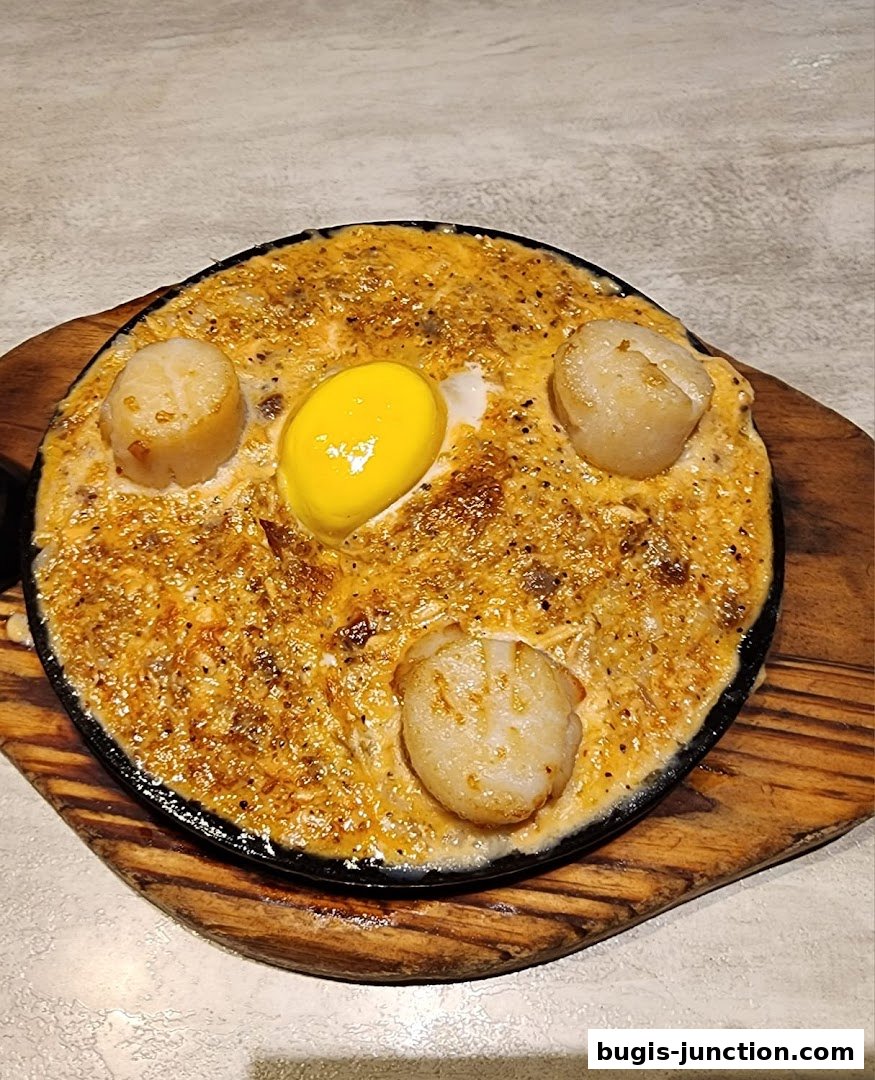 A sizzling dish with scallops and a fried egg in a creamy sauce.