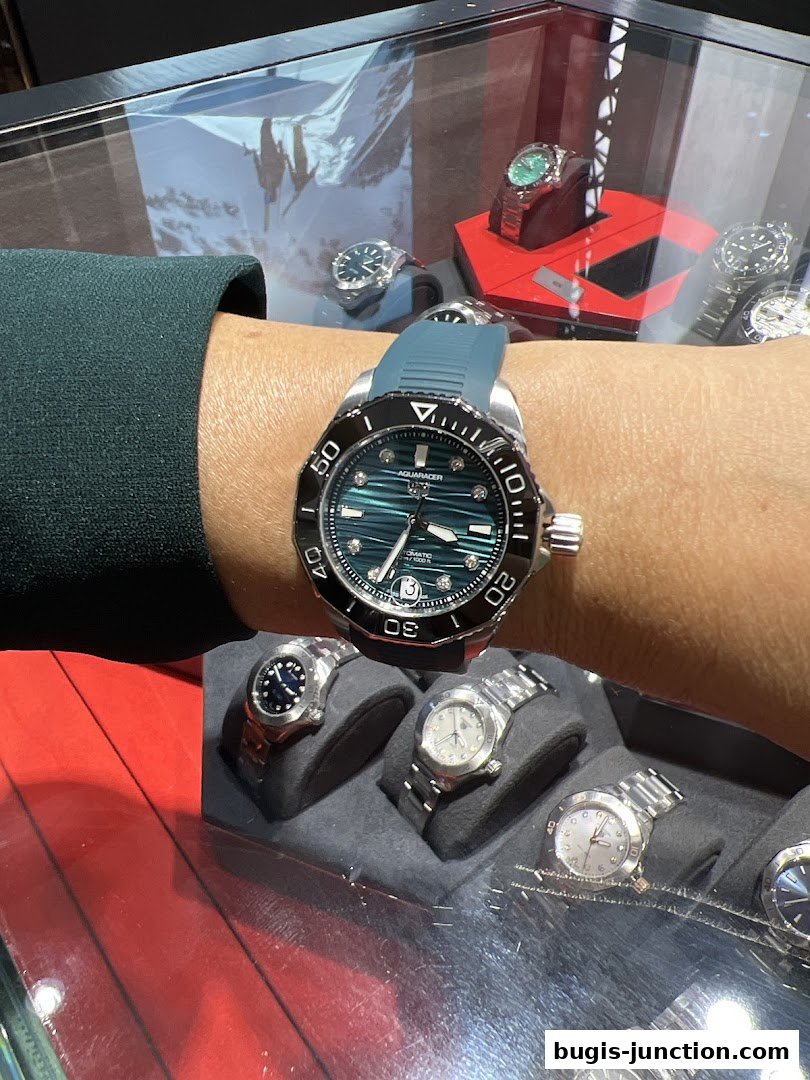 A person wearing a stylish watch, with a display of various watches in the background.