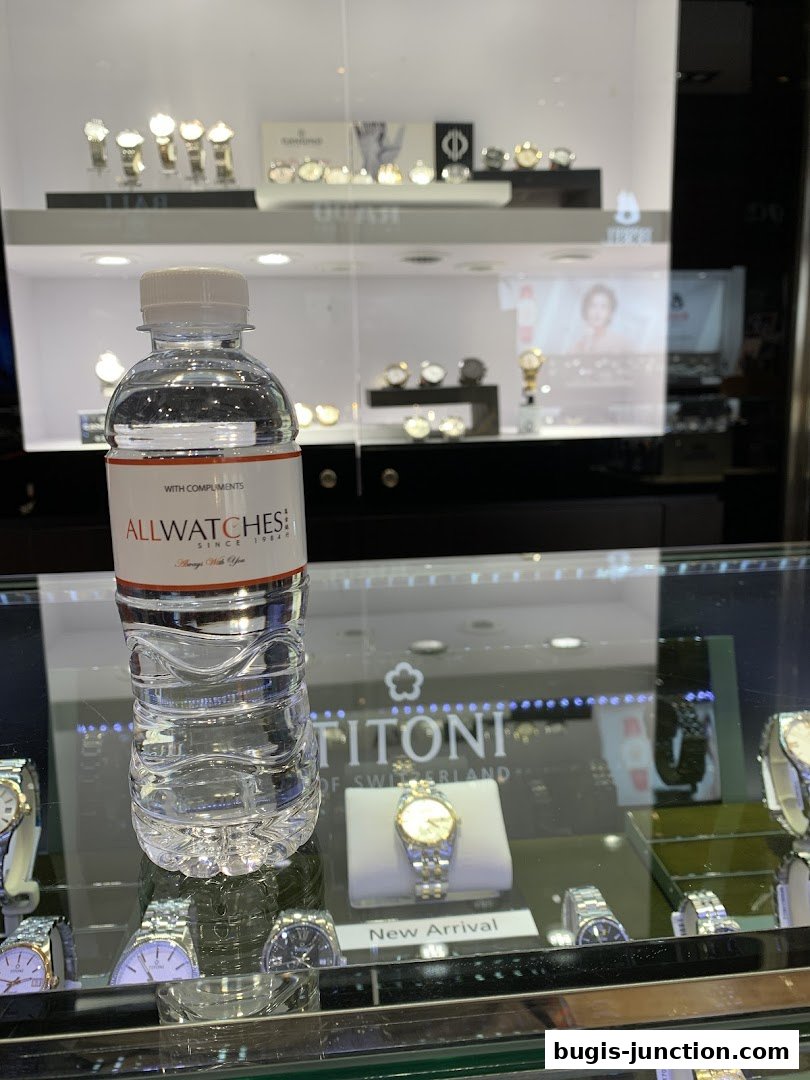 A bottle of water with the "All Watches" logo in front of a display of watches.