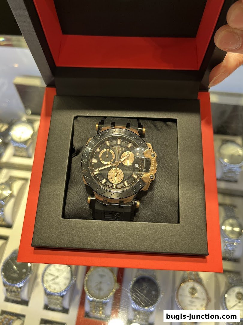A luxury watch displayed in an open red and black box, with other watches visible in the background.