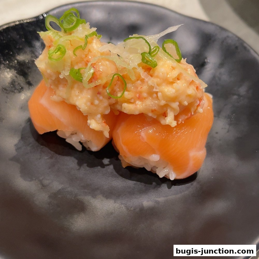 Two pieces of salmon sushi with a creamy topping and green onions on a black plate.