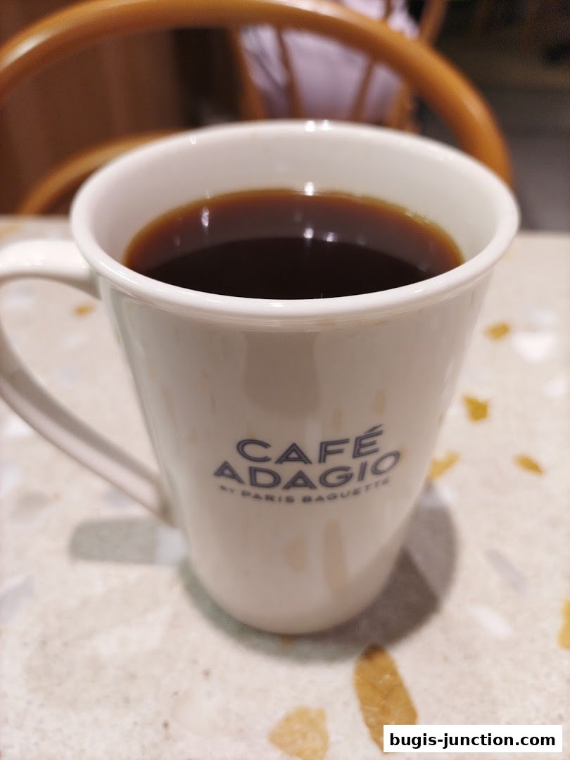 A close-up shot of a white mug filled with dark coffee, with the cafe's logo visible.