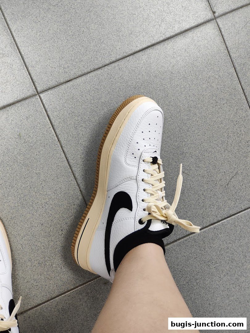 A person wearing white Nike Air Force 1 sneakers with cream laces and a gum sole.
