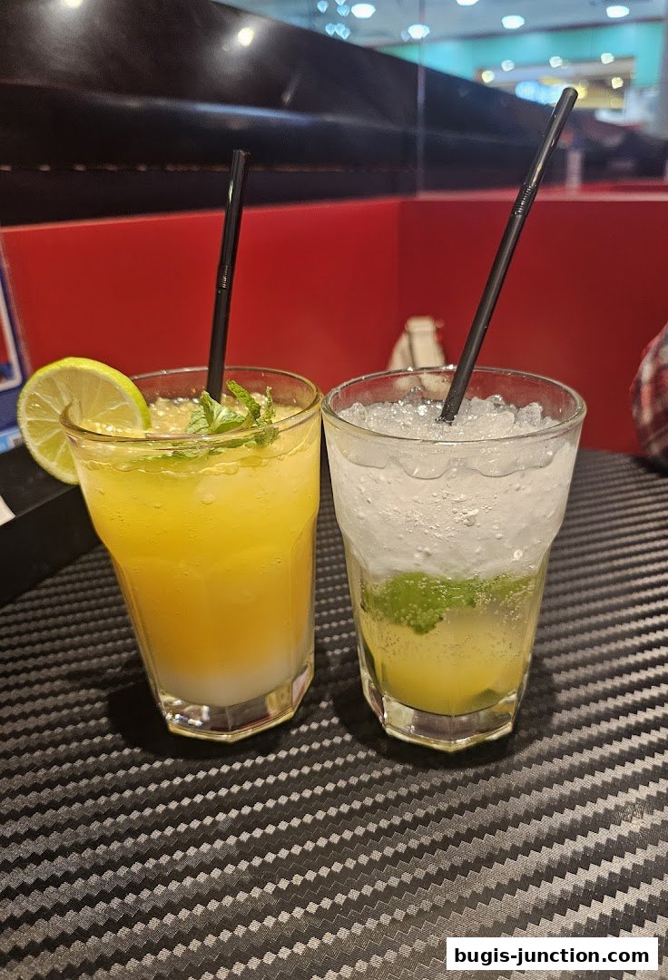 Two refreshing drinks, one orange and one clear with mint and lime, served with straws.