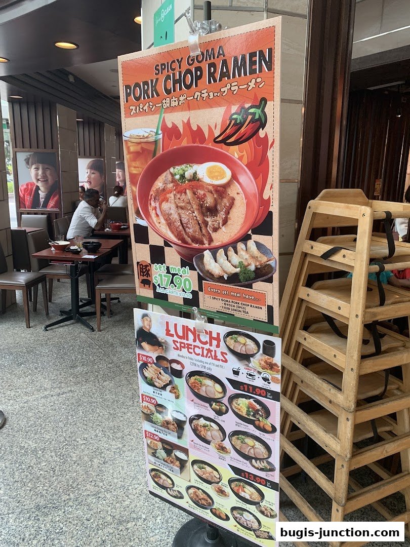 A sign advertising Ajisen Ramen's Spicy Goma Pork Chop Ramen and lunch specials.