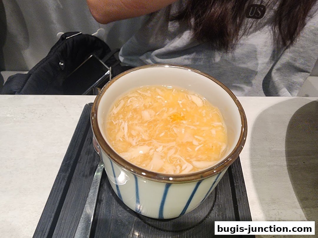 A close-up of a bowl of soup with shredded chicken and egg.