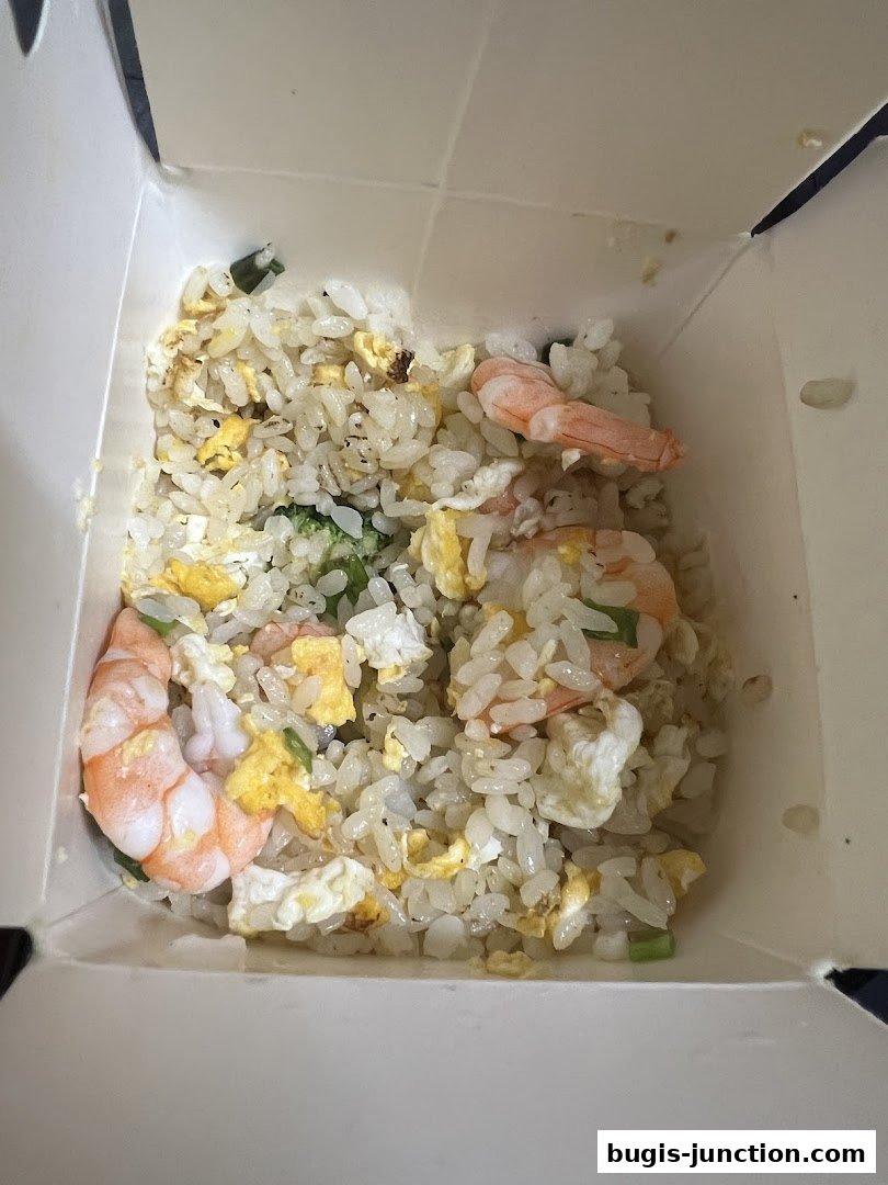 A close-up of shrimp fried rice in a takeout container with visible shrimp, egg, and green onions.