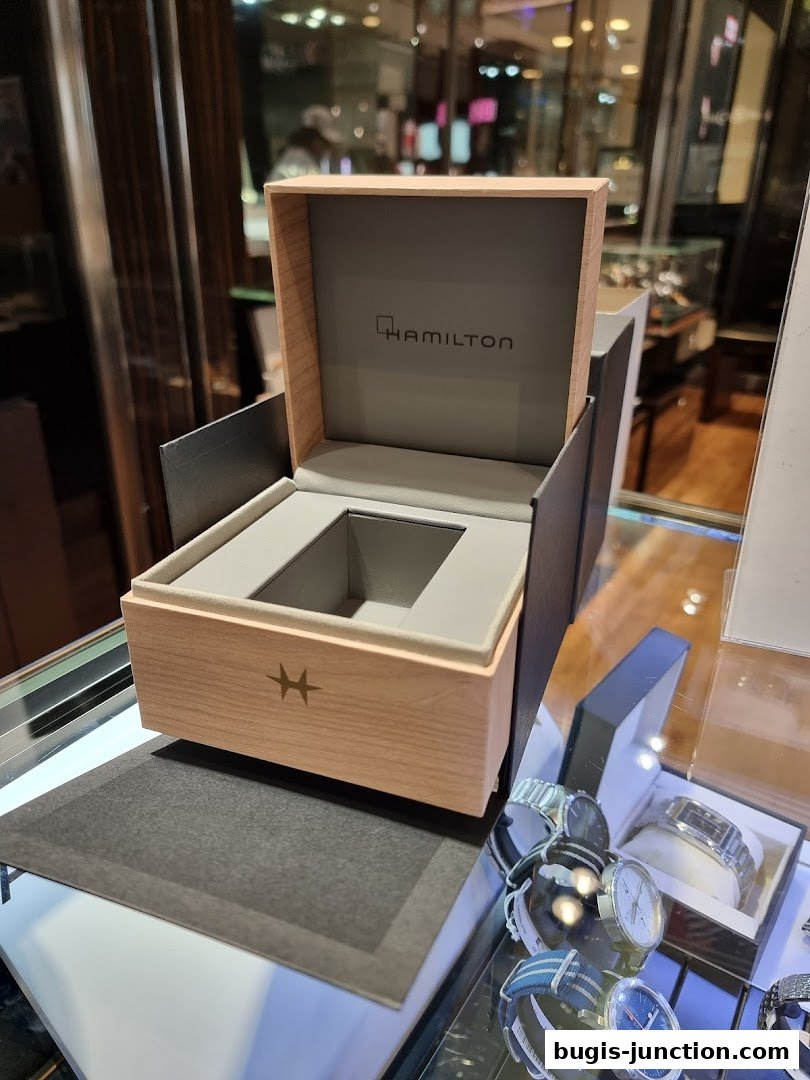 A Hamilton watch box is open, displaying the brand logo, with watches in a display case.