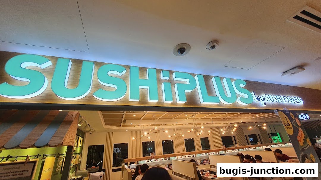 The illuminated sign for Sushi Plus, a sushi restaurant, is prominently displayed above the entrance.