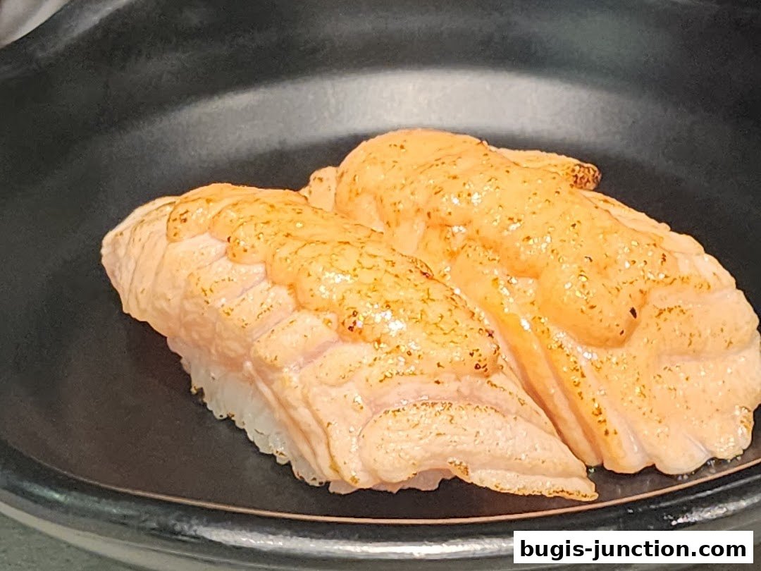 Close-up of two pieces of salmon sushi with a creamy topping on a black plate.