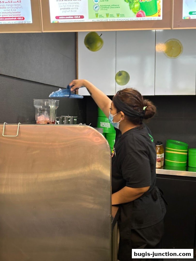 A Boost Juice employee prepares a drink behind the counter, adding ice to a blender.
