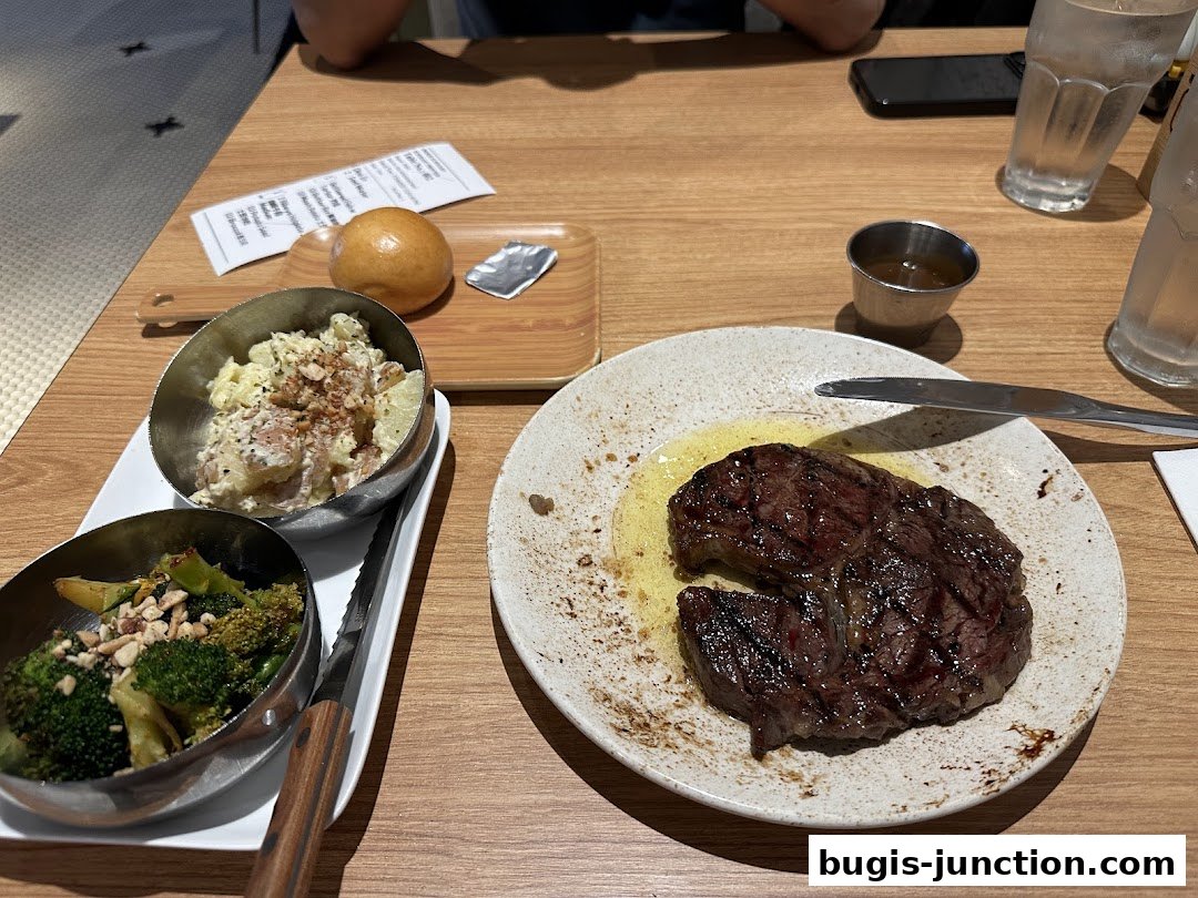 A grilled steak with sides of potato salad and broccoli is served on a wooden table.