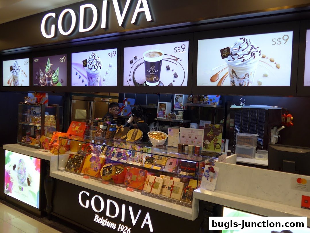 A Godiva chocolate shop counter displaying various chocolate boxes and promotional images of desserts.