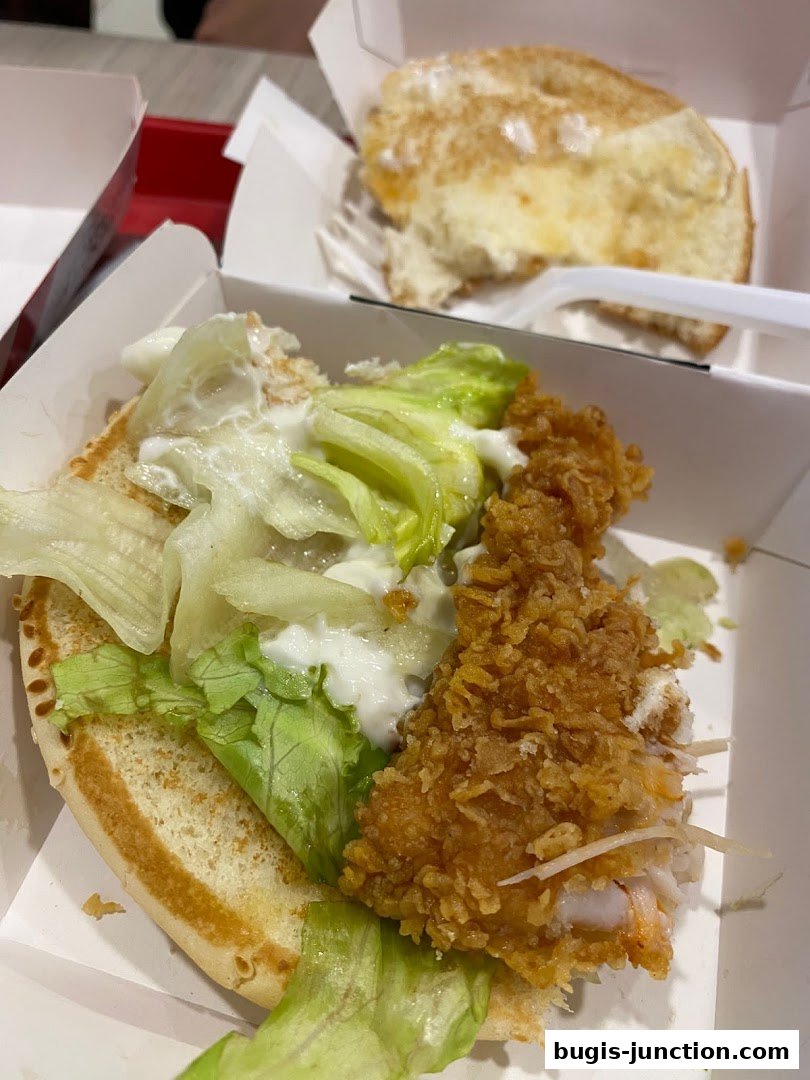 A close-up of a KFC chicken burger with lettuce and sauce in a white box.
