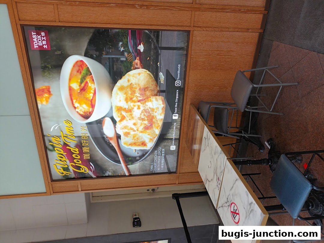 A promotional poster for Toast Box featuring curry chicken with prata and seating area.
