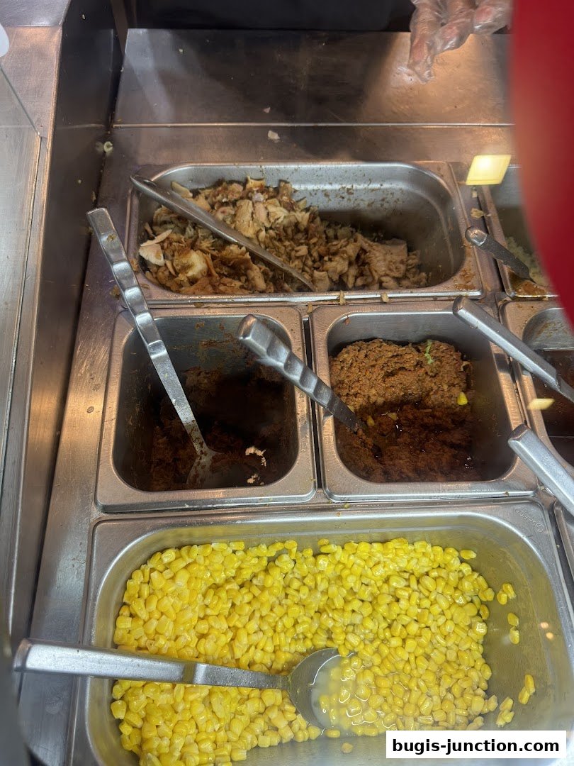 A close-up of a food service counter with various ingredients in metal trays.