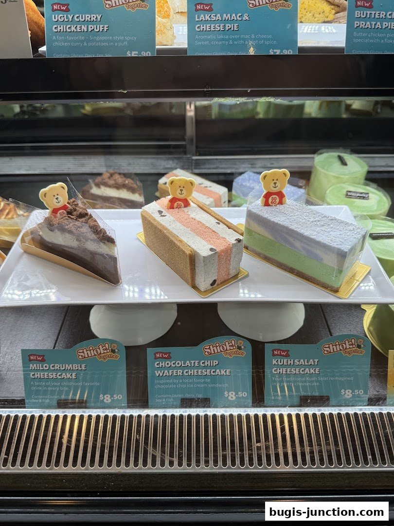A display case filled with various cheesecakes and pastries, each with a descriptive label.