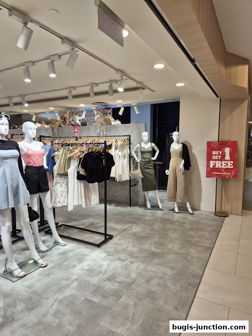 Mannequins display stylish outfits inside a clothing store with racks of apparel.