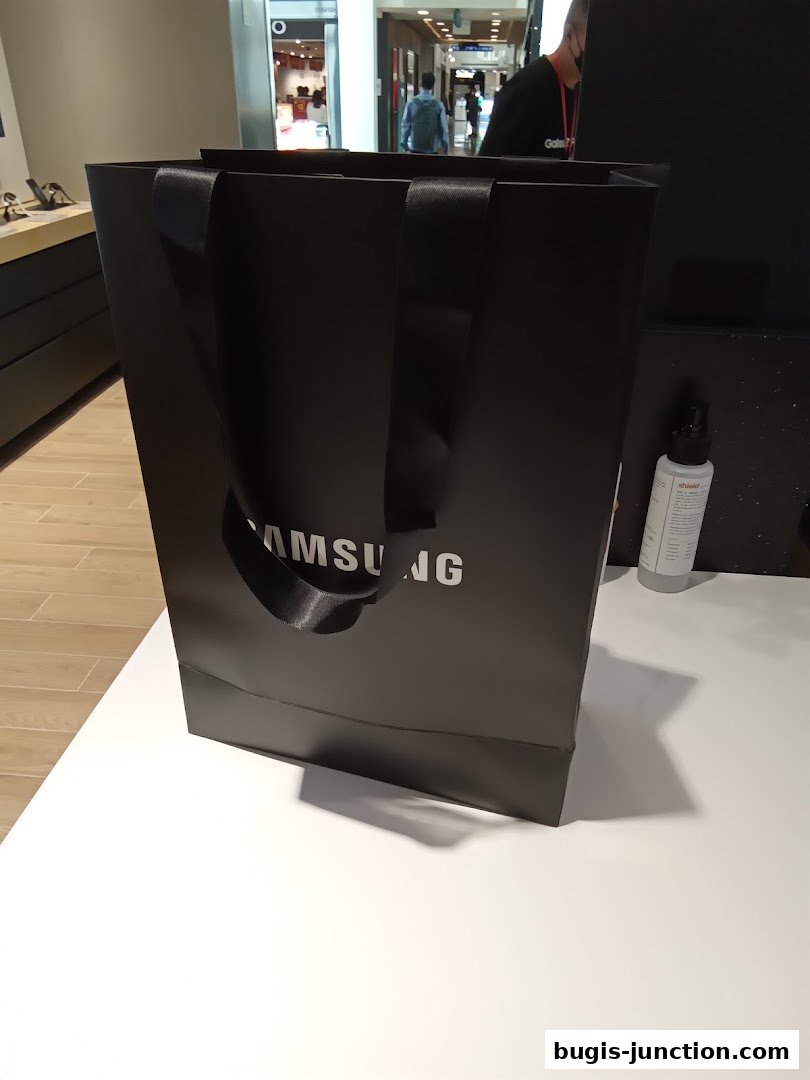 A black Samsung shopping bag with white lettering sits on a white table.