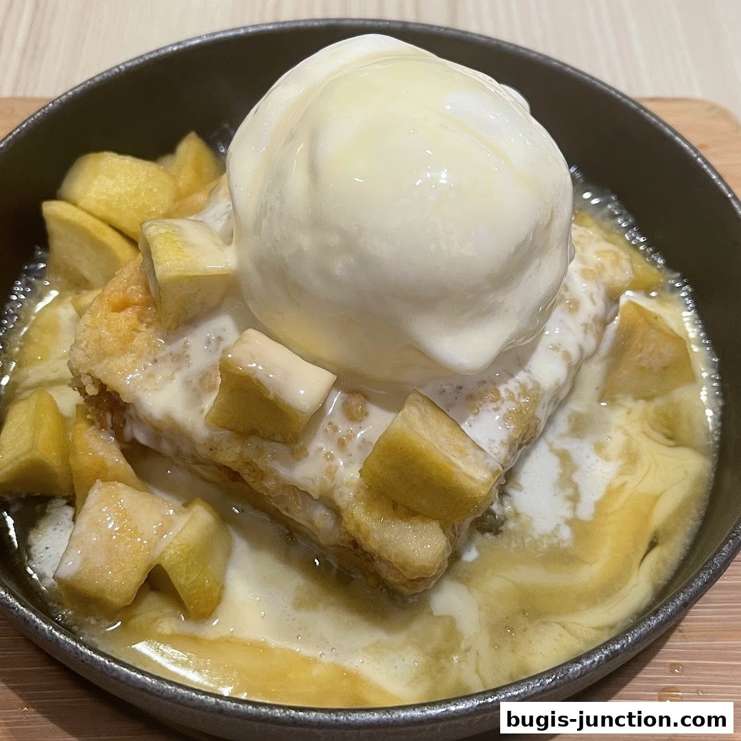A warm apple crumble dessert topped with vanilla ice cream and drizzled with sauce.