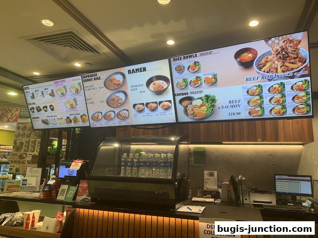 A digital menu board displaying various Japanese food items like ramen, curry rice, and beef bowls.