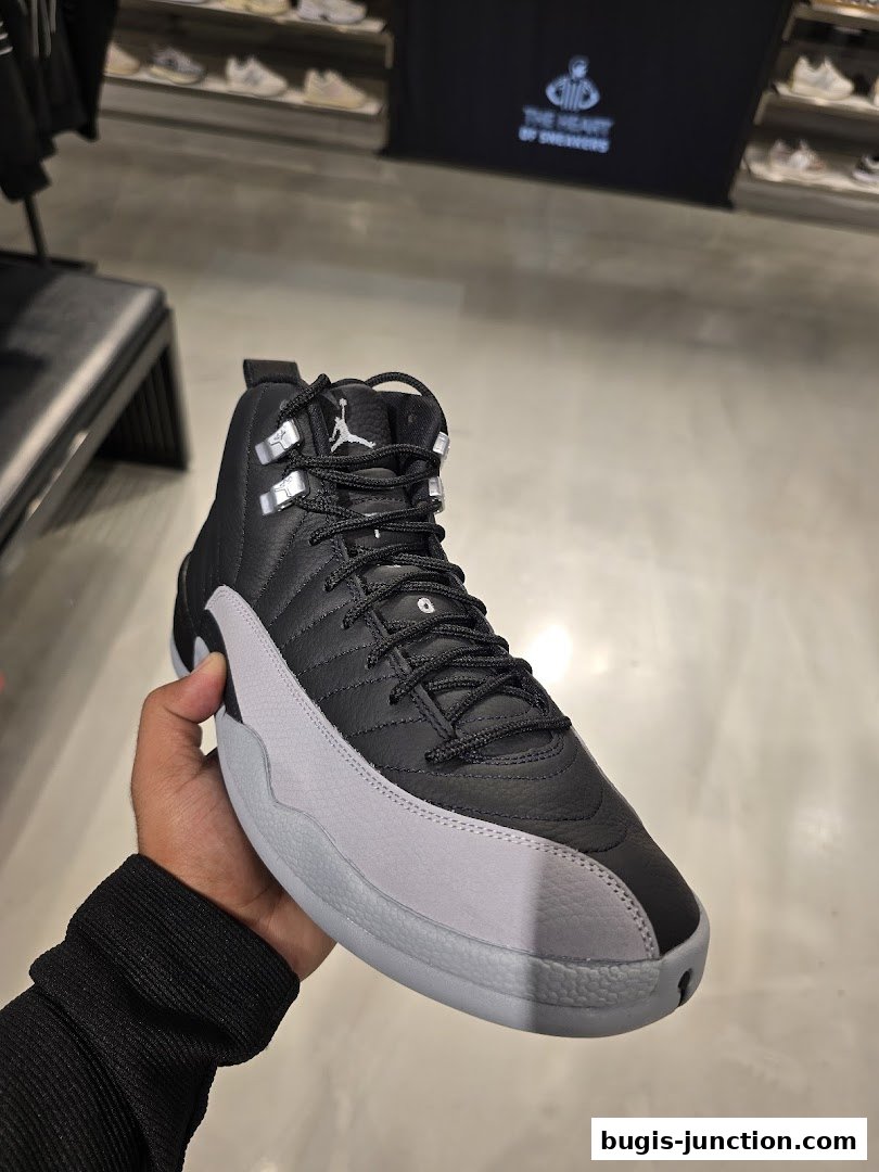 A hand holds a black and grey Nike Air Jordan 12 sneaker in a retail store.