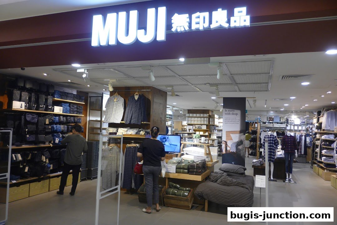 Interior view of a MUJI store showcasing clothing, bags, and bedding with customers browsing.