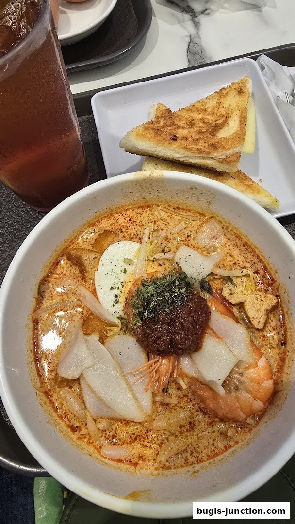 A bowl of Laksa with toast and iced tea, a popular Southeast Asian dish.