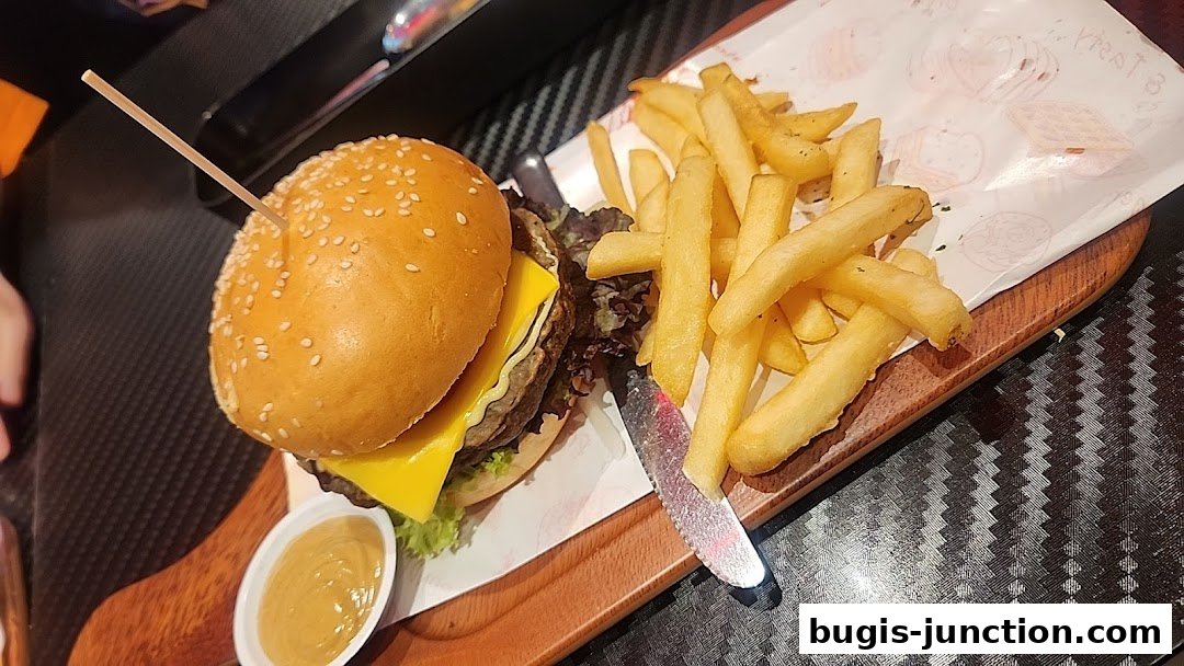 A juicy burger with cheese and fries served on a wooden board with a side of sauce.