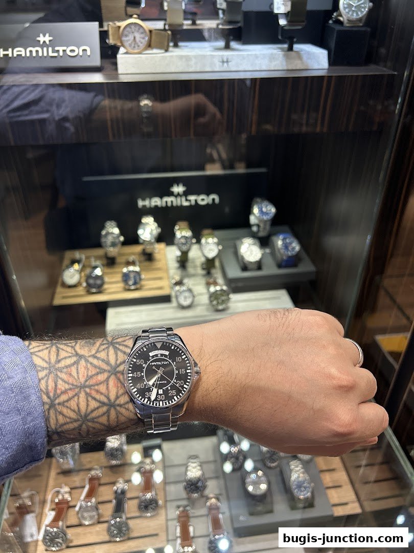 A person's arm wearing a Hamilton watch in front of a display of watches.