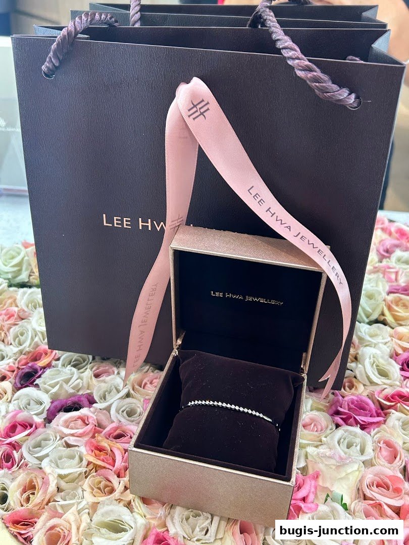 A Lee Hwa Jewellery gift bag and open jewelry box with a diamond bracelet on a bed of roses.