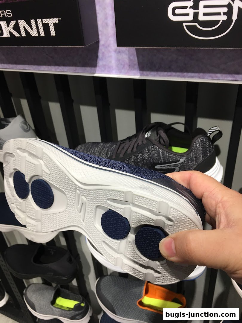A hand holds a Skechers shoe, showcasing its sole with visible cushioning technology.
