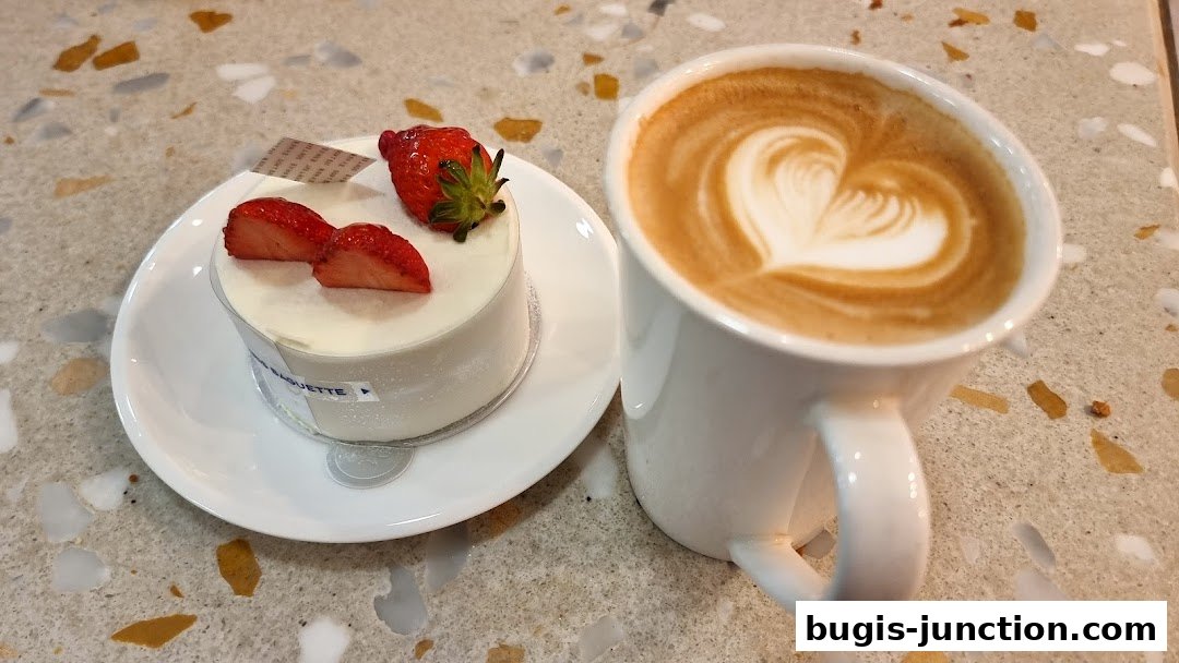 A delicate strawberry cake and a latte with heart art sit on a speckled countertop.