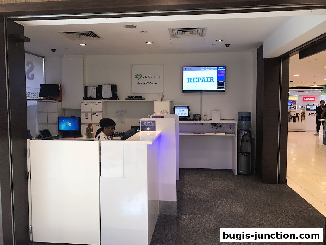 A service counter with a person working, computers, and a 'REPAIR' sign on a screen.