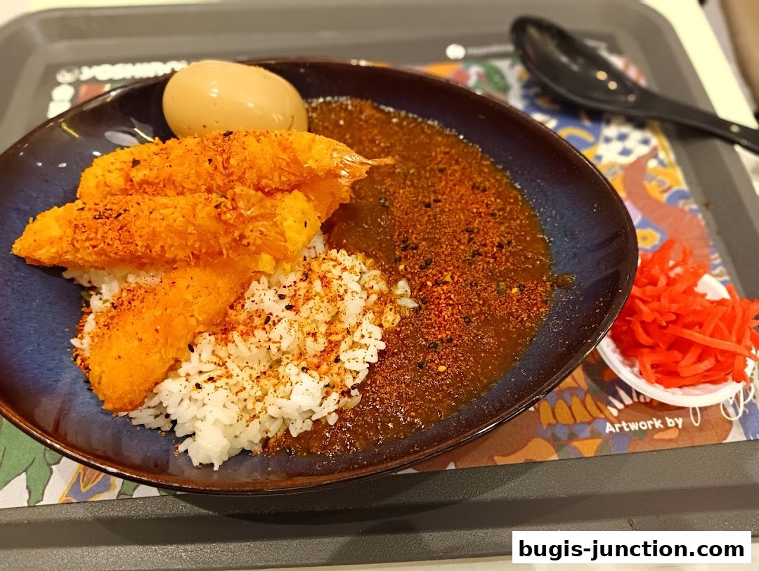 A close-up of a Yoshinoya dish featuring crispy fried shrimp, rice, curry, and a boiled egg.