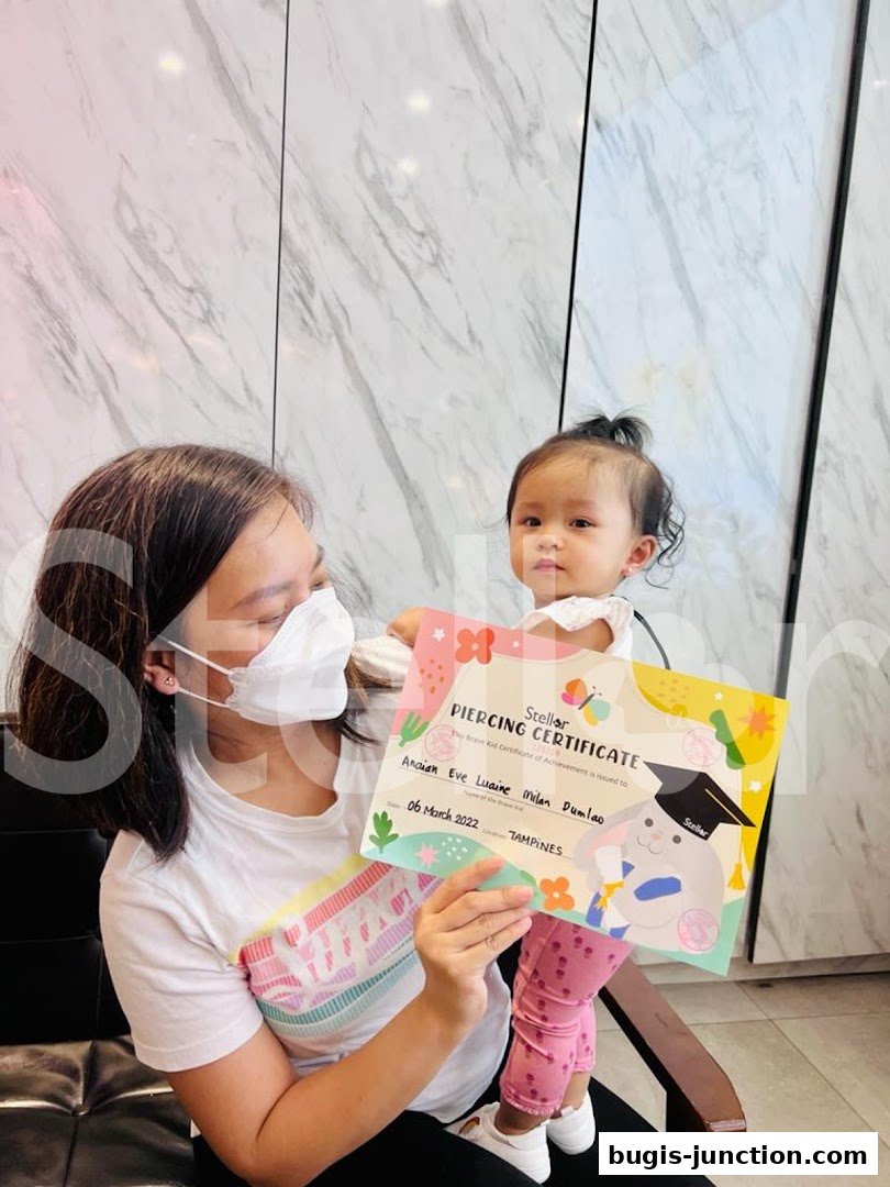 A woman holds a piercing certificate with a baby in her arms.