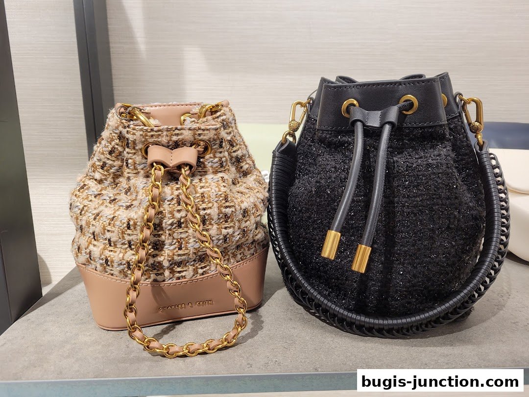 Two stylish bucket bags, one in tweed and the other in black sequins, displayed on a shelf.