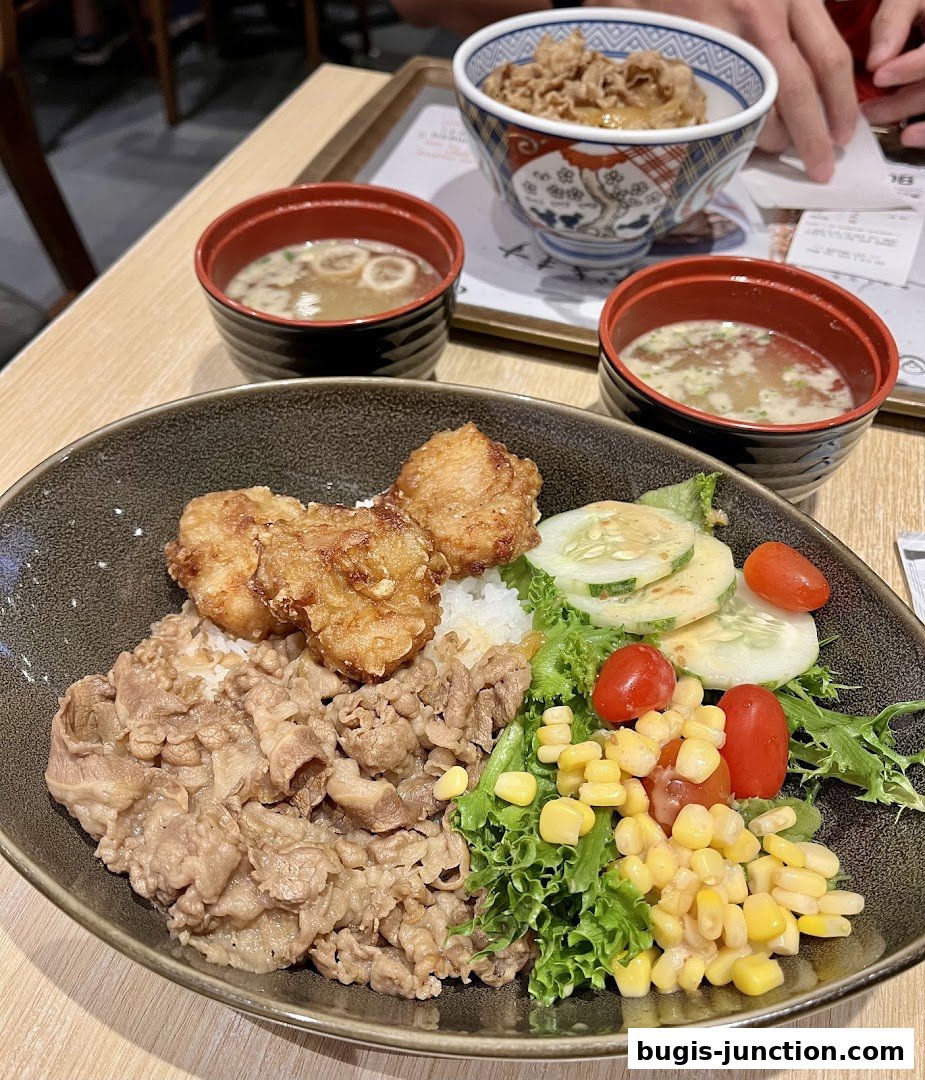 A close-up of a Yoshinoya meal featuring beef bowl, fried chicken, and miso soup.