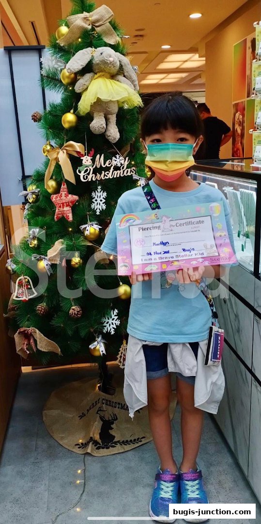 A child holds a piercing certificate in front of a decorated Christmas tree.