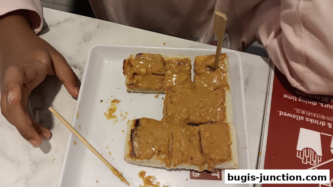 A plate of toast with peanut butter is served with a wooden skewer.