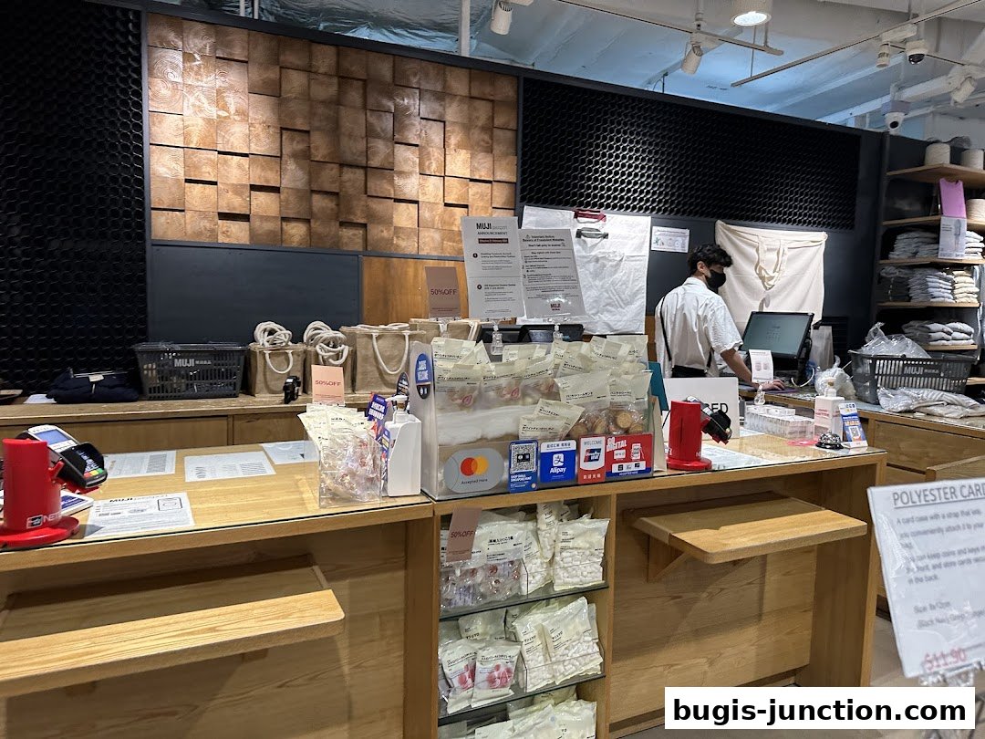 A cashier at MUJI Bugis Junction stands behind a counter with various products and payment terminals.