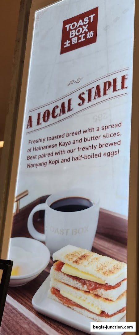 A sign for Toast Box featuring their signature kaya toast, coffee, and half-boiled eggs.