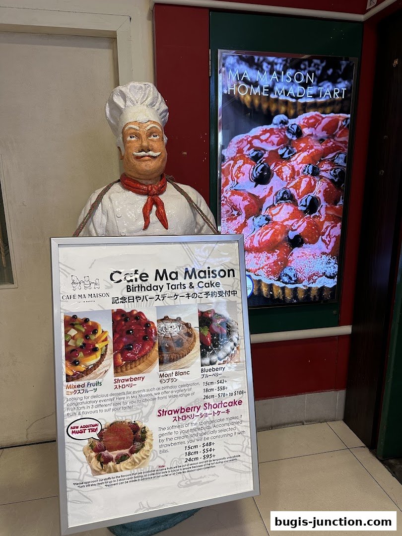 A chef statue stands in front of a display of tarts and cakes from Cafe Ma Maison.