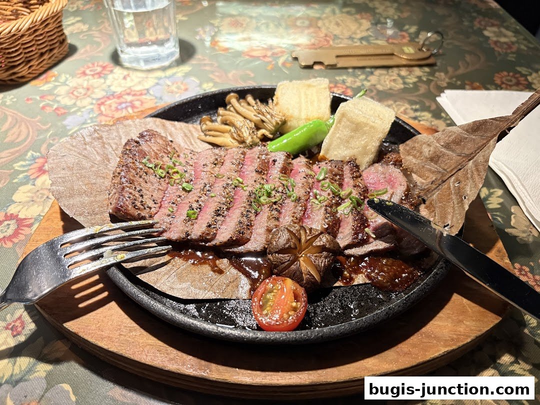 A sliced steak dish served on a sizzling plate with mushrooms, peppers, and a tomato.