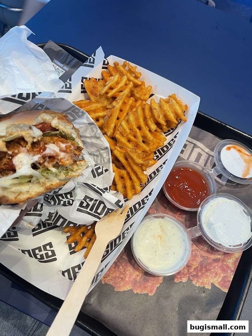 A delicious-looking burger and waffle fries served with dipping sauces on a tray.