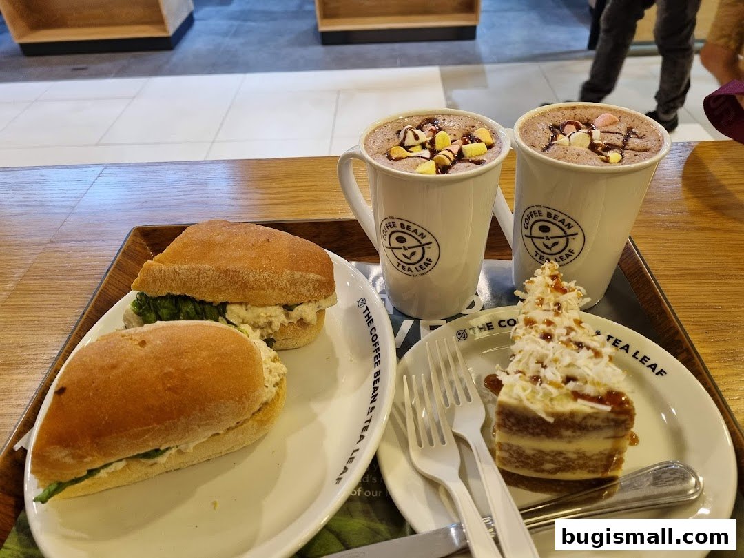 Two hot beverages with marshmallows, two sandwiches, and a slice of cake on a tray.