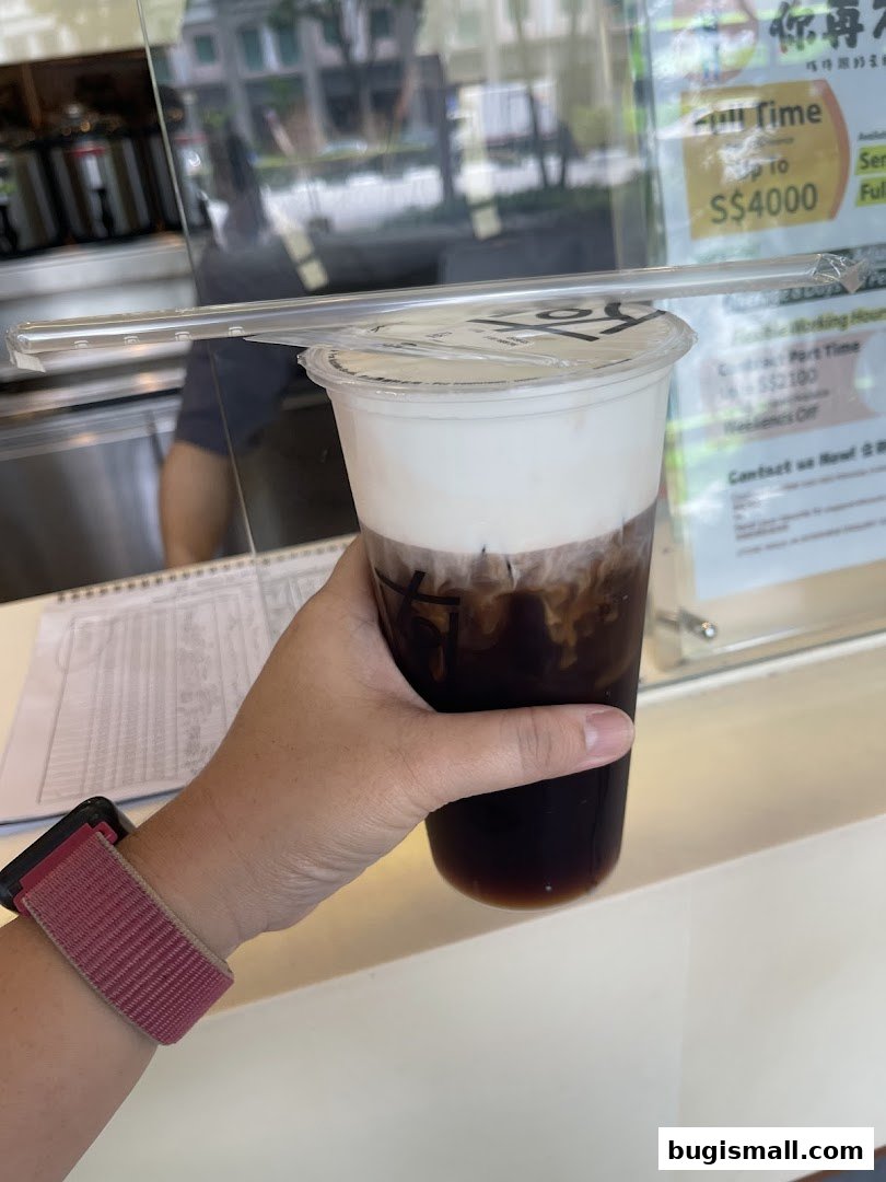 A hand holds a KOI Thé drink with a creamy top and dark liquid.